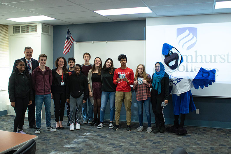 一群Willowbrook高中学生与Elmhurst学院校长Troy Vanaken和Mascot Victor E. Bluejay合影。